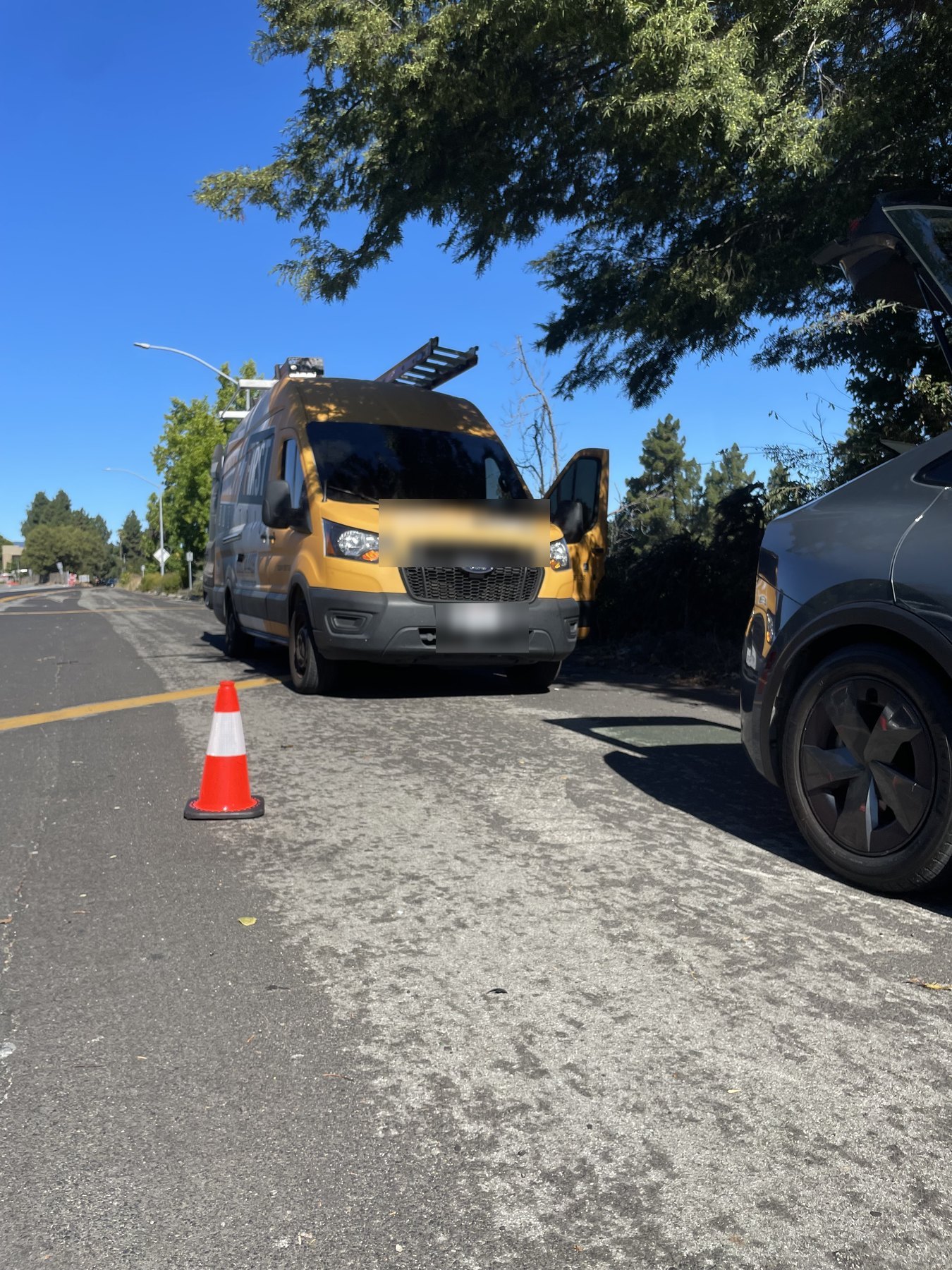 A work van pulled over on a tree-lined street during a roadside tire call