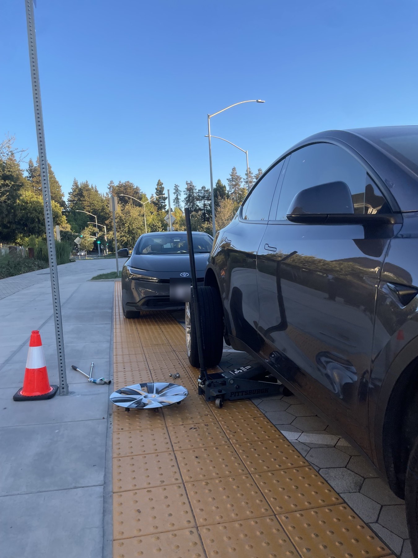 A Tesla raised on a floor jack at the curb with the wheel removed