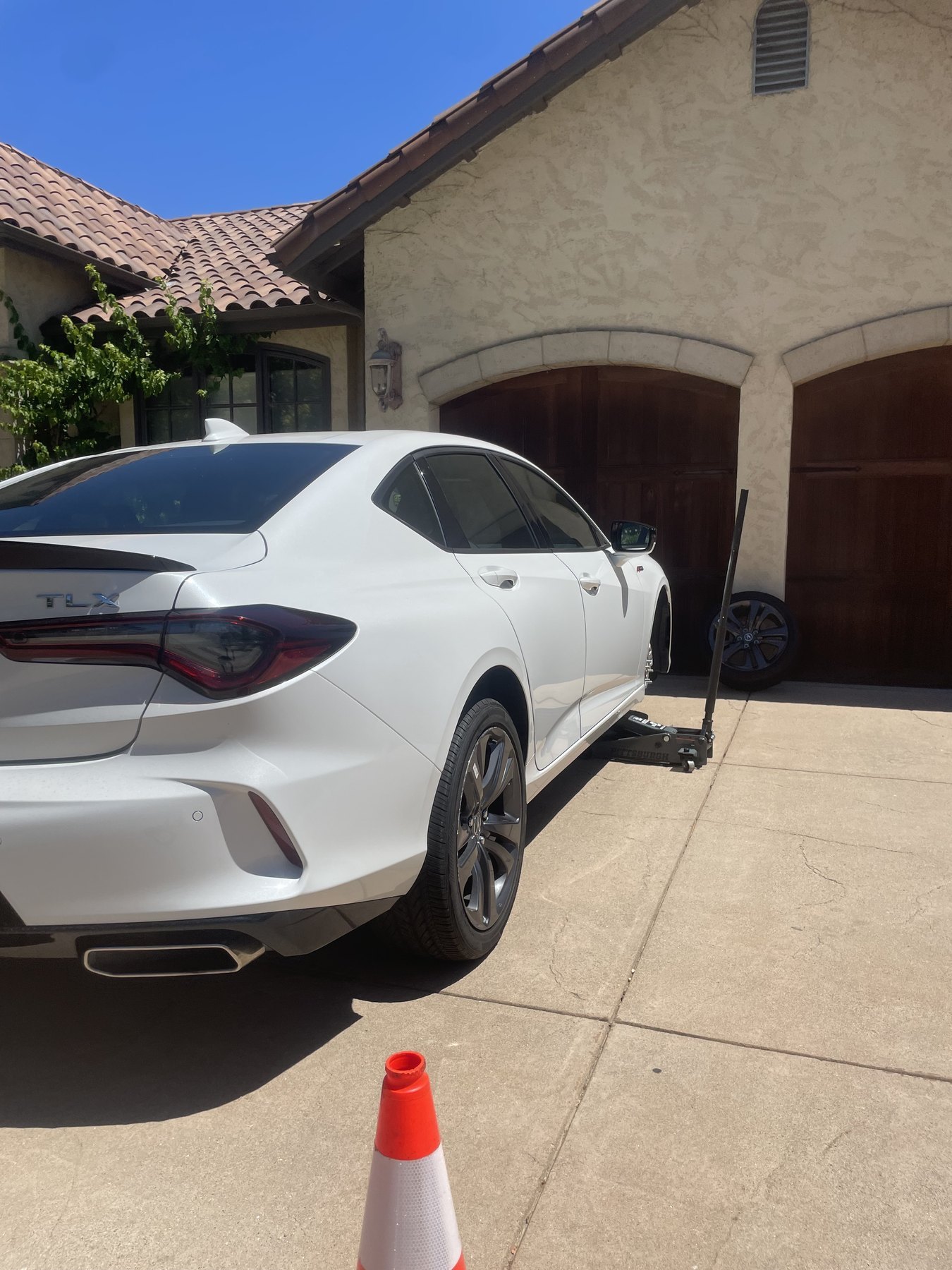 A white sedan raised on a floor jack in a driveway during a mobile tire service call