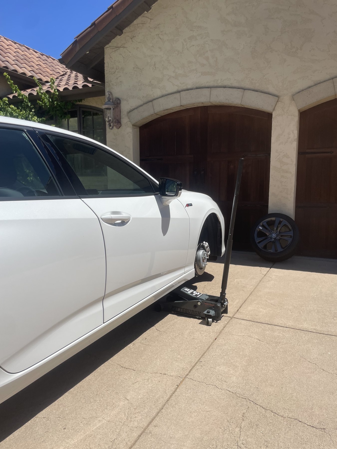 A white sedan on a floor jack with the wheel removed during a roadside tire change