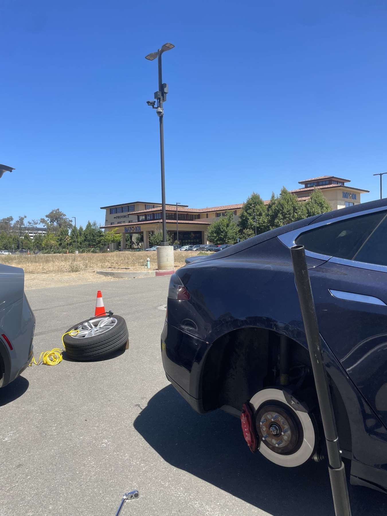 A car with the rear wheel removed and the spare on the ground in a parking lot