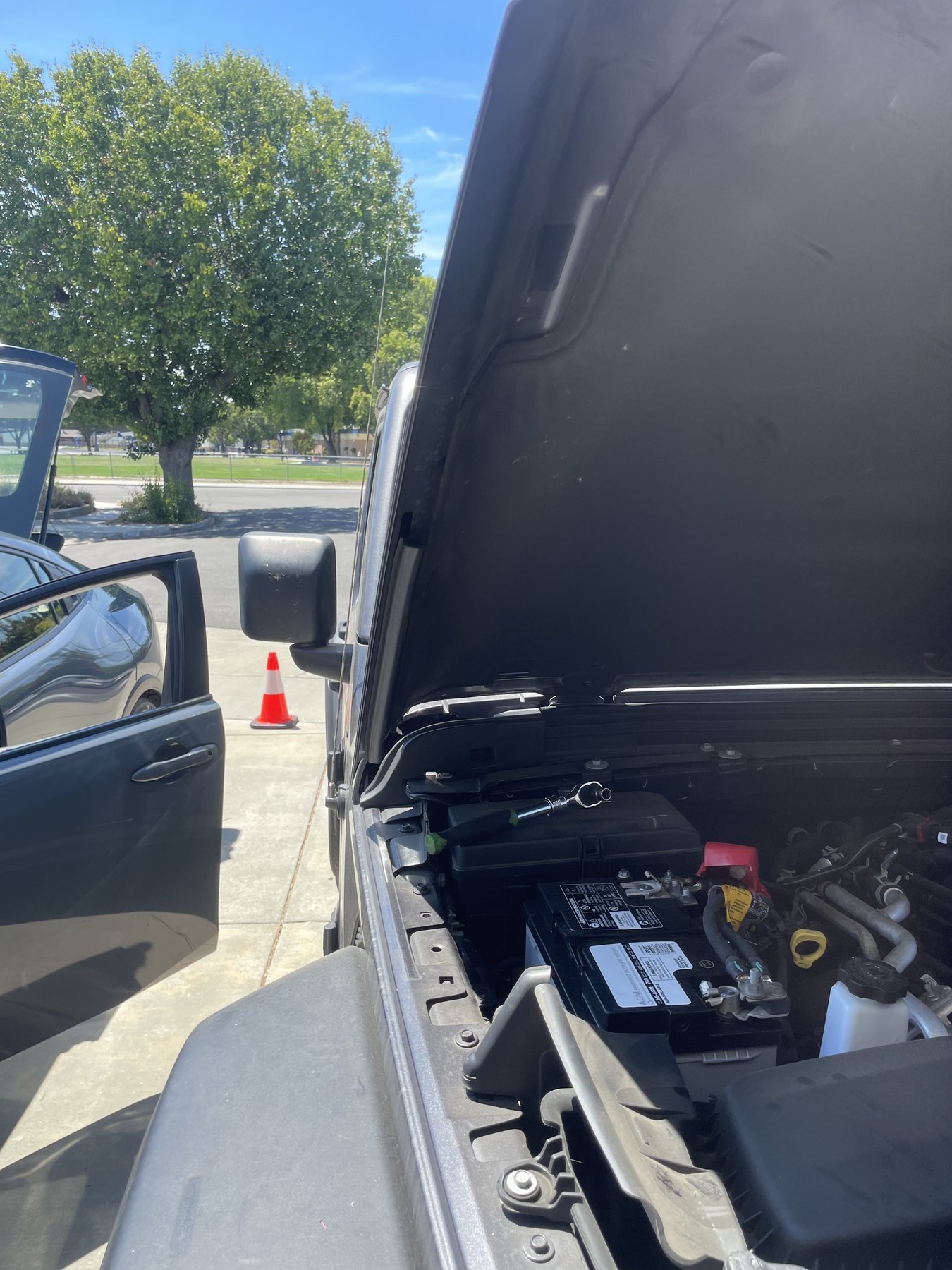 A Jeep with the hood up and a new battery being fitted at the roadside
